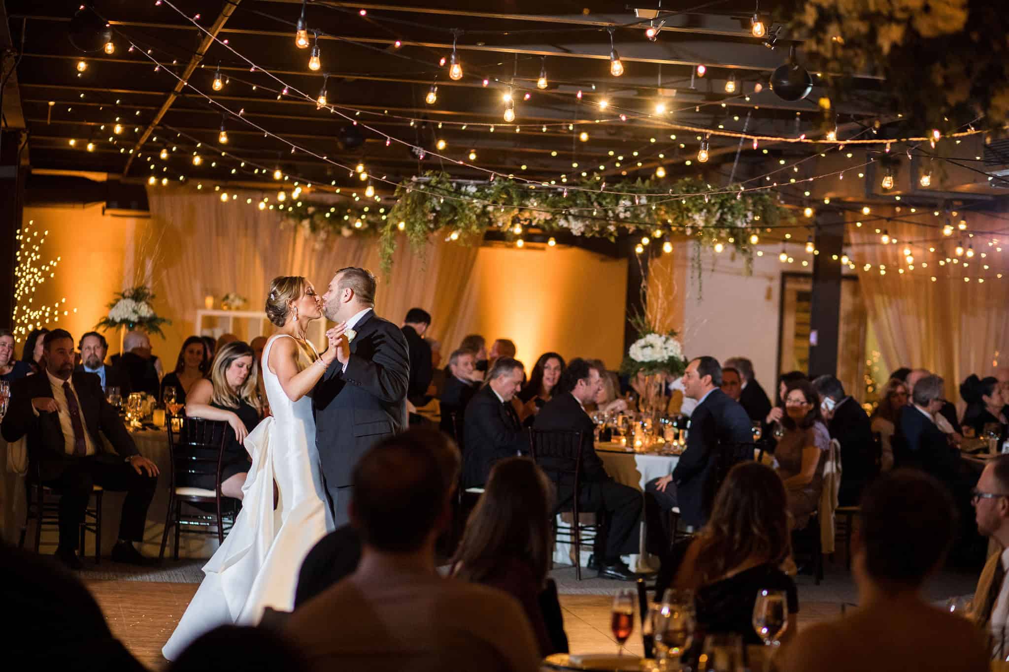 Couple dancing at SKY Armory reopening celebration with guests and string lights.