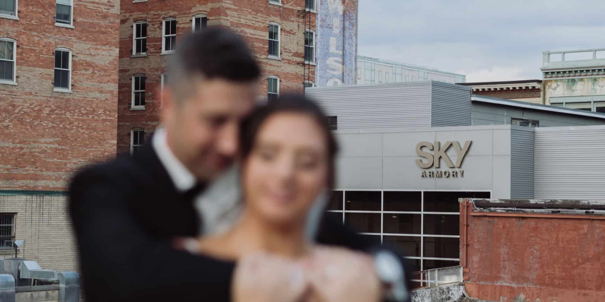 Couple at Sky Armory wedding venue with cityscape background.