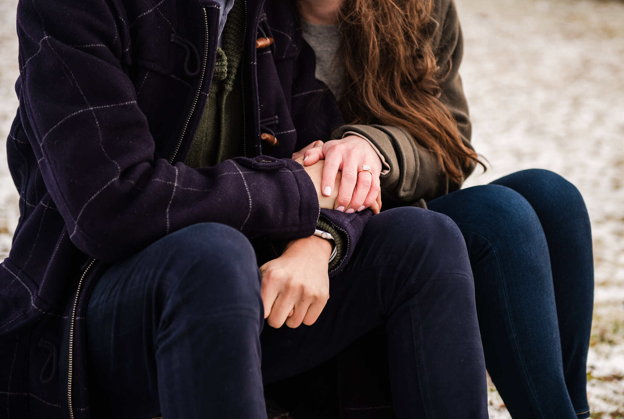 Close-up of a couple holding hands while sitting outdoors in cold weather.