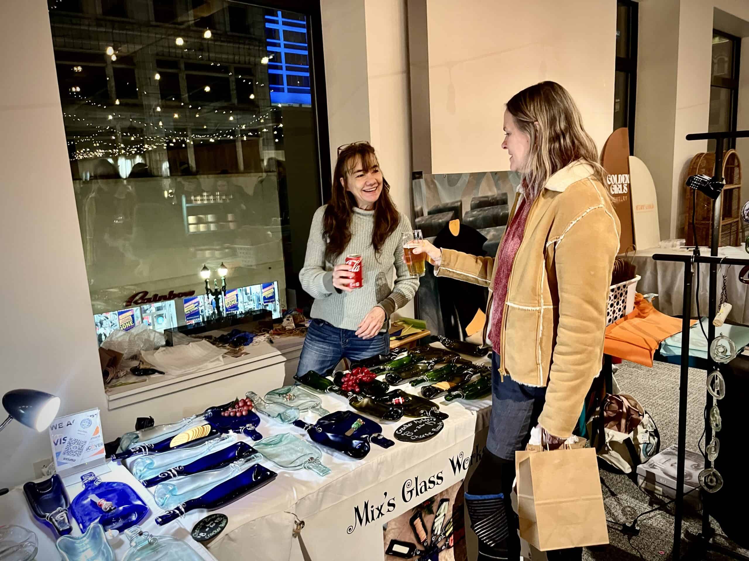 Two women exchanging drinks at SKY Armory glassware booth.