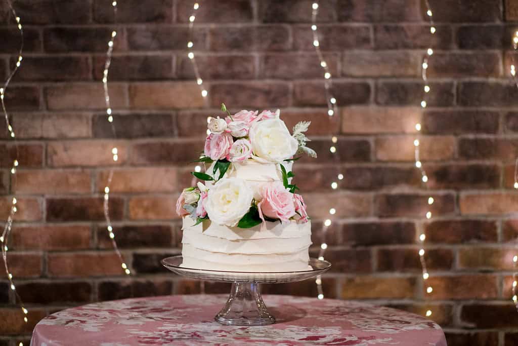 Beautiful wedding cake decorated with pink and white roses on a glass stand.