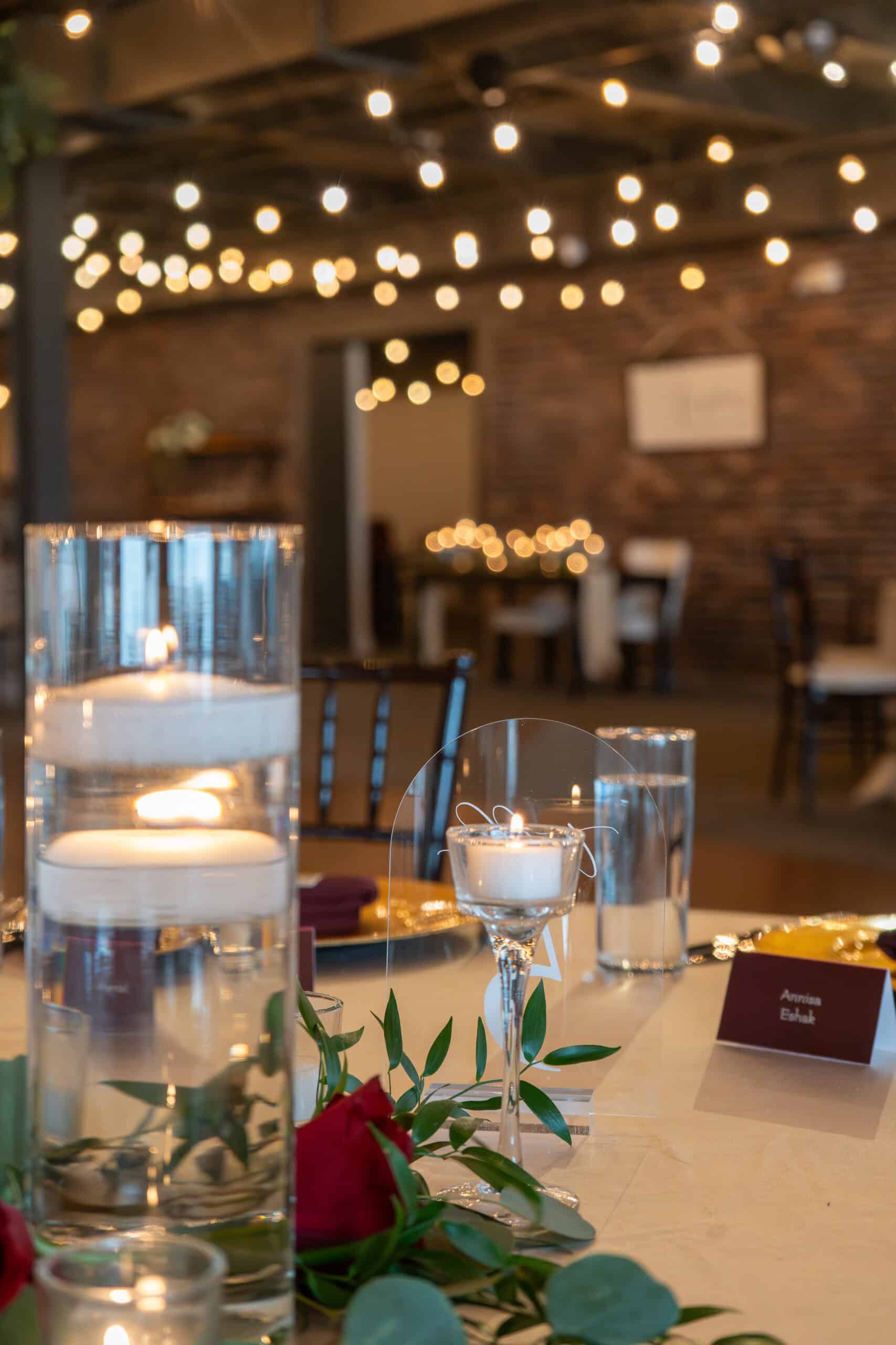 Wedding reception table with candles and string lights in a rustic venue.