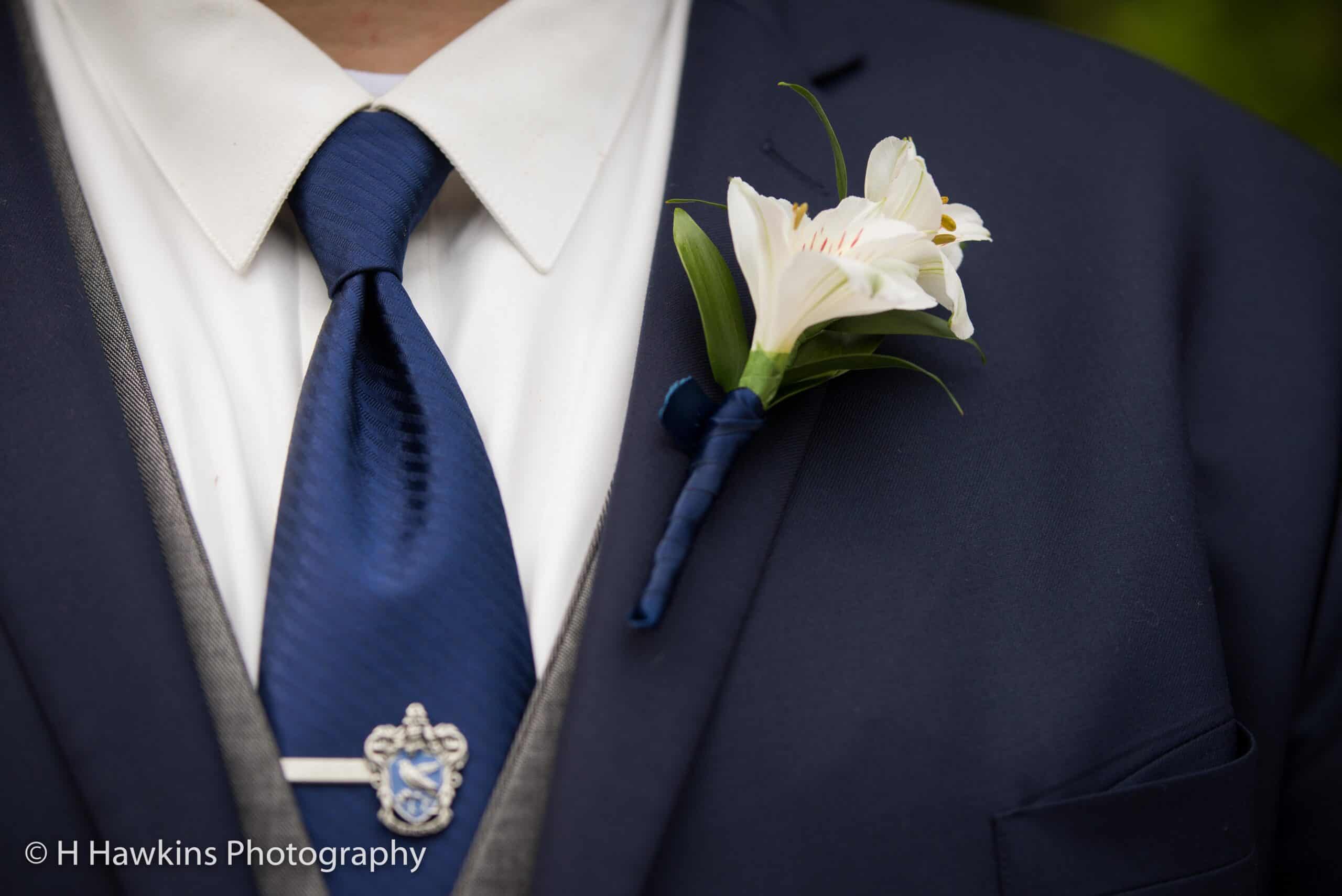 Close-up of groom's navy suit with white lily boutonniere and blue tie.