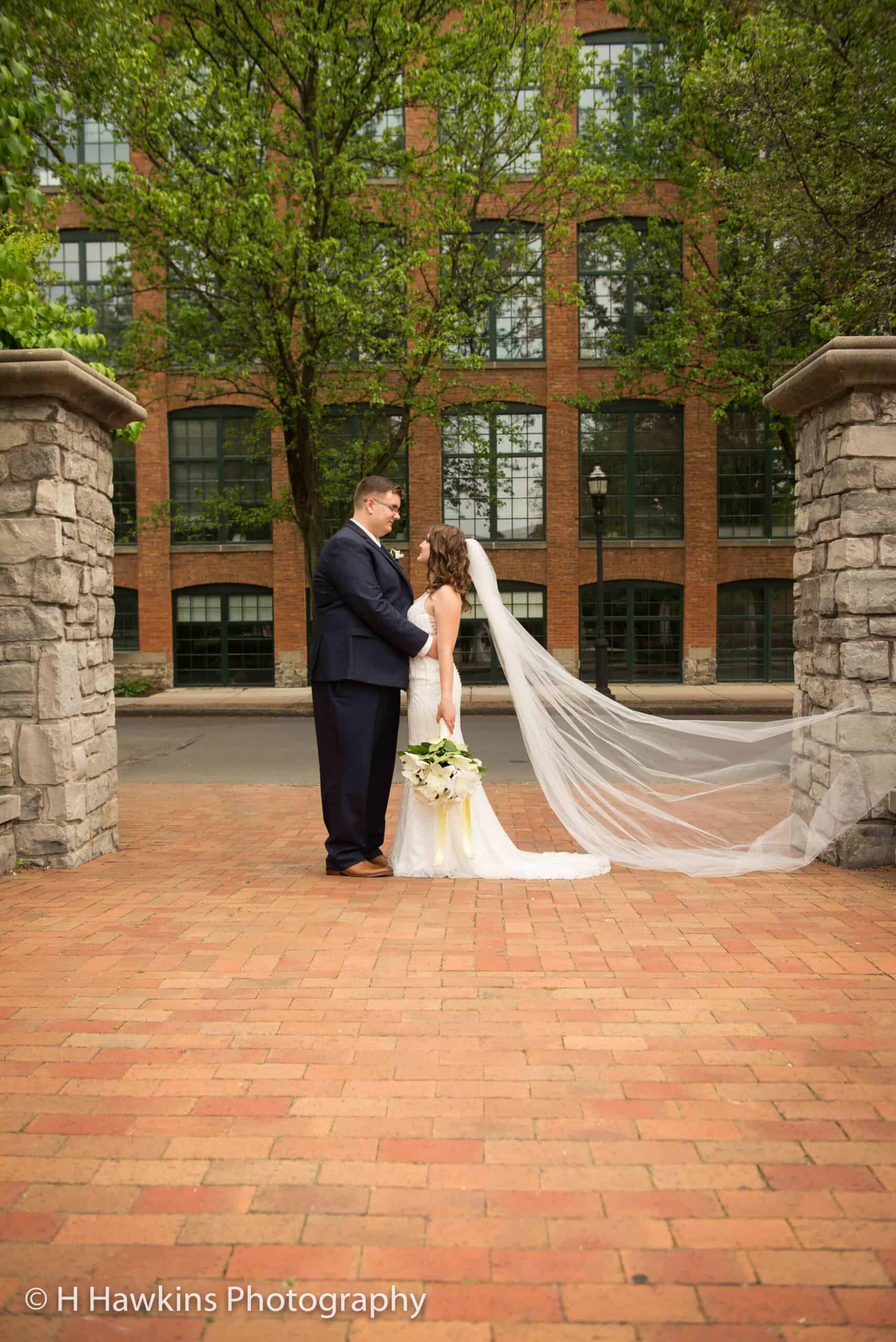 Bride and groom holding hands outdoors with cityscape background.