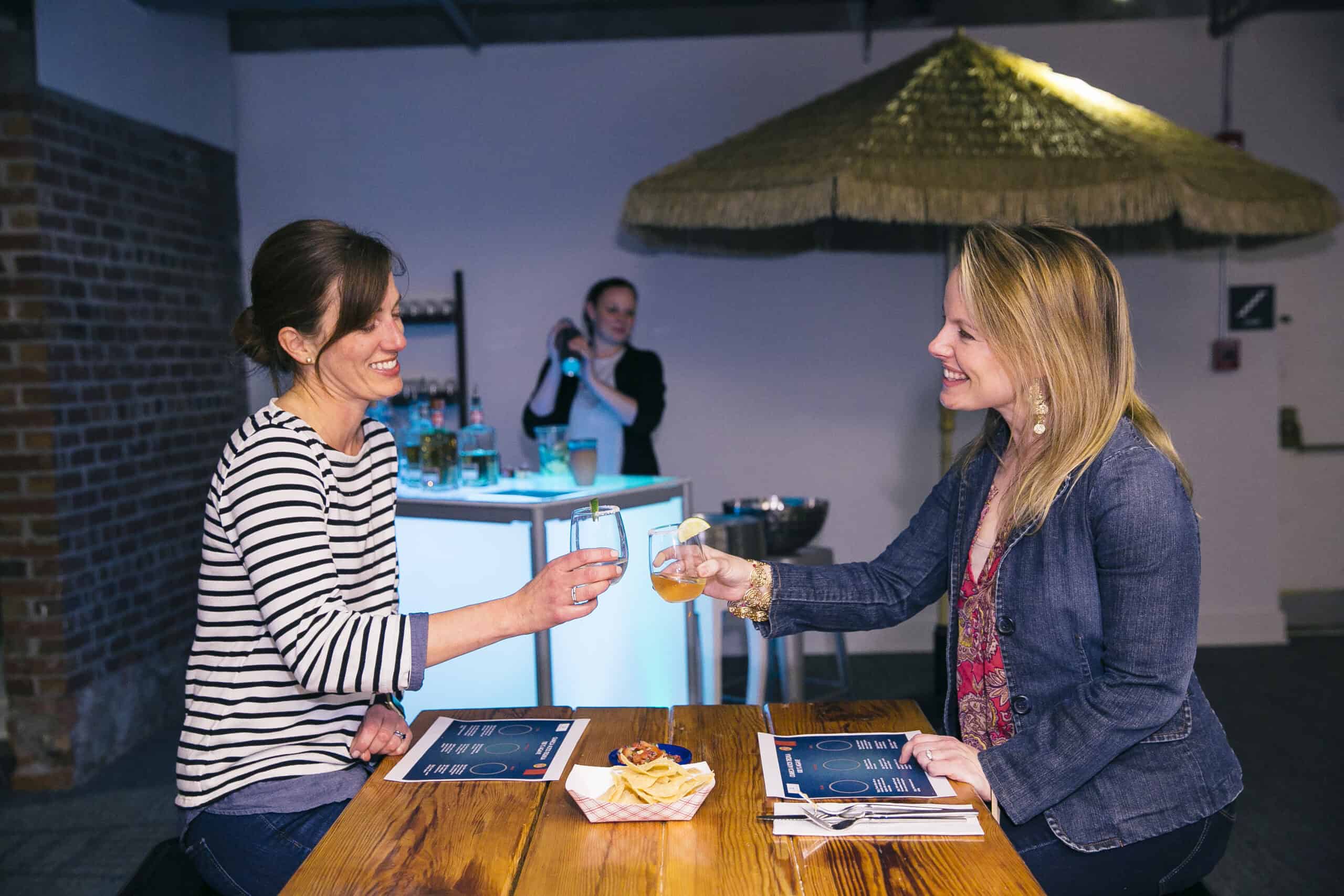 Two women enjoying drinks at Sky Armory event with a bartender in the background.