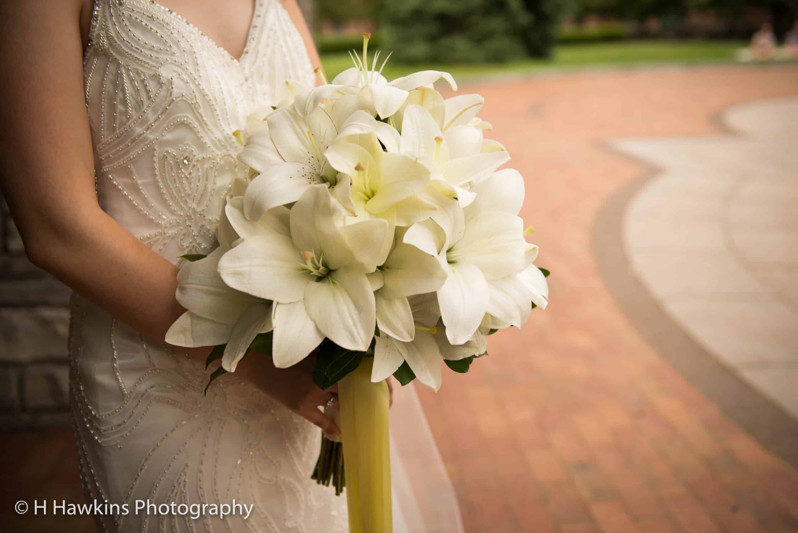 Bride holding a beautiful white lily bouquet outdoors.