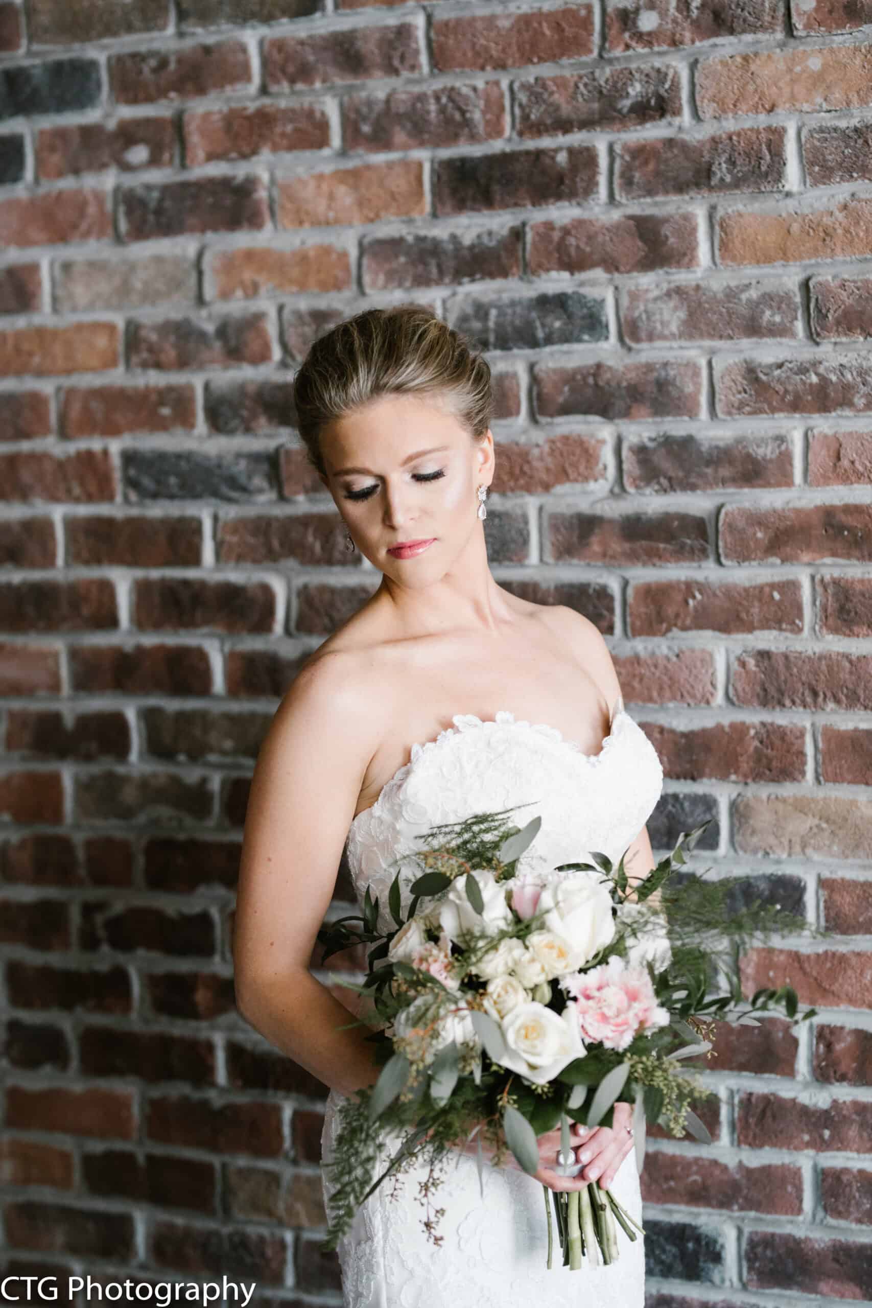 Bride holding a bouquet of white and pink roses against a brick wall.