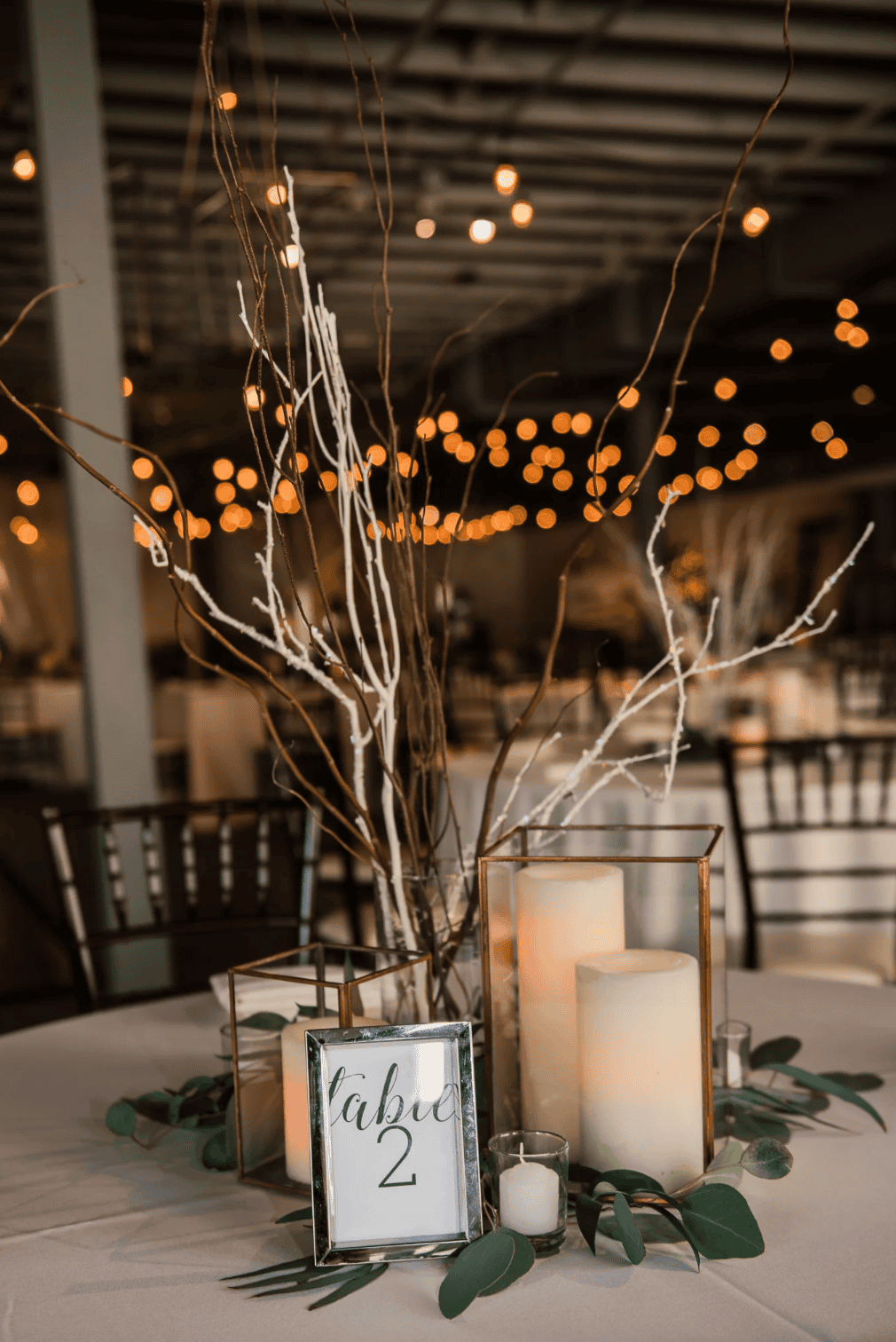 Decorative table centerpiece with candles, branches, and greenery for event decor.