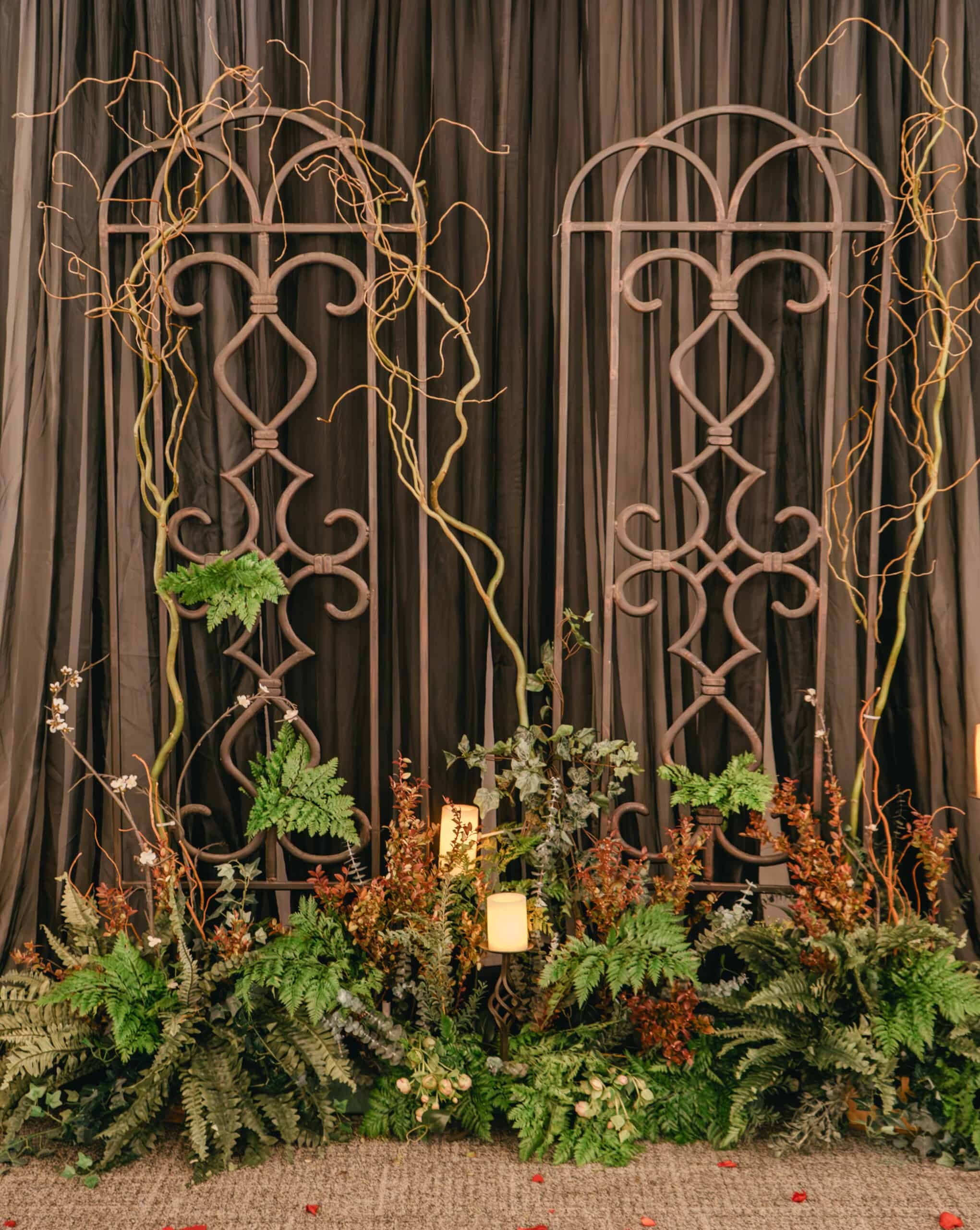 Decorative wedding backdrop with iron arches, greenery, and candles.