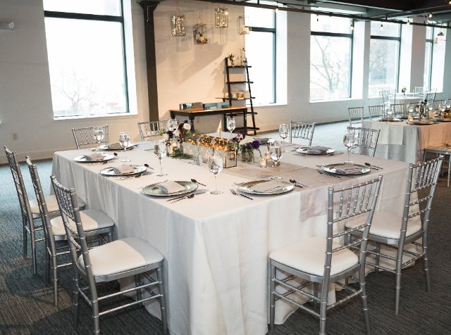 Beautifully decorated wedding reception table with silver chairs and floral centerpieces.