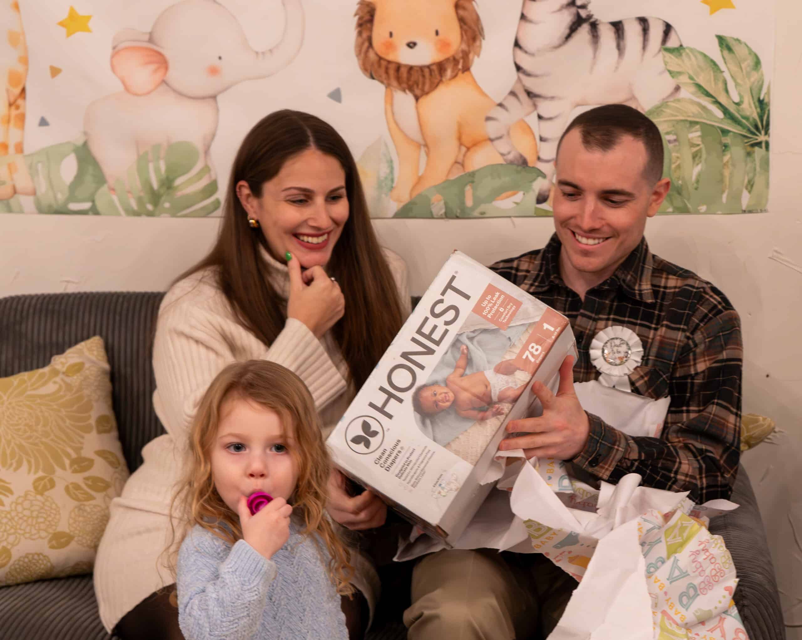 Happy family opening a baby shower gift at a venue with jungle animal decor.