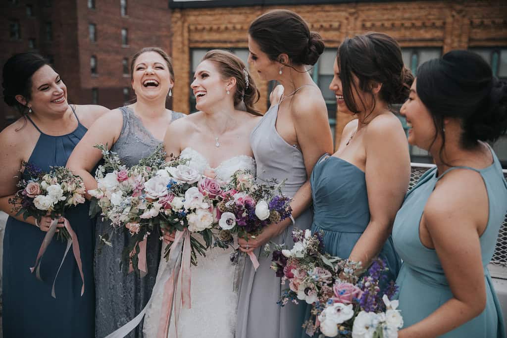 Group of bridesmaids in different pastel dresses holding bouquets at wedding.