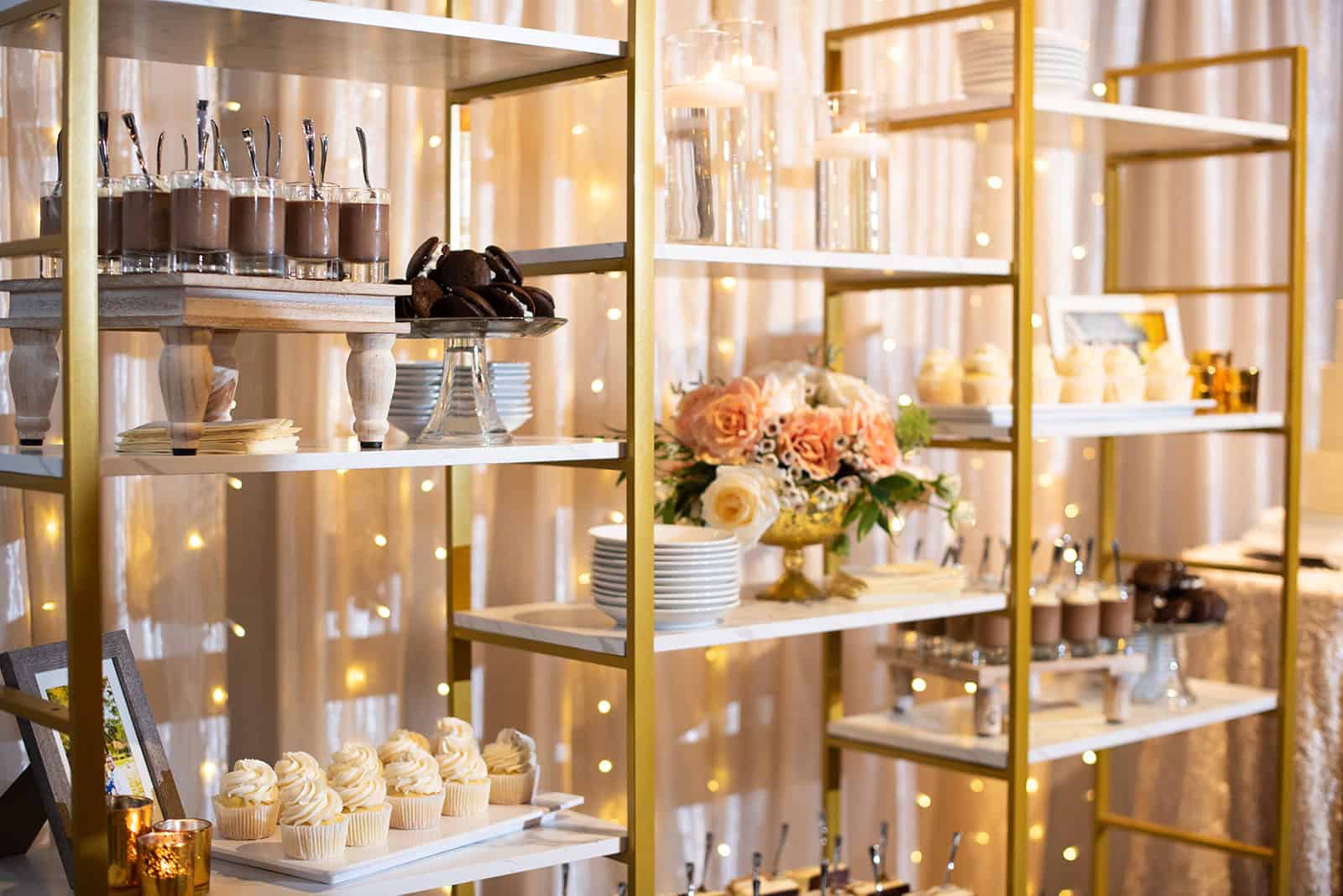 Dessert table with cupcakes, chocolates, and floral arrangements at a wedding.
