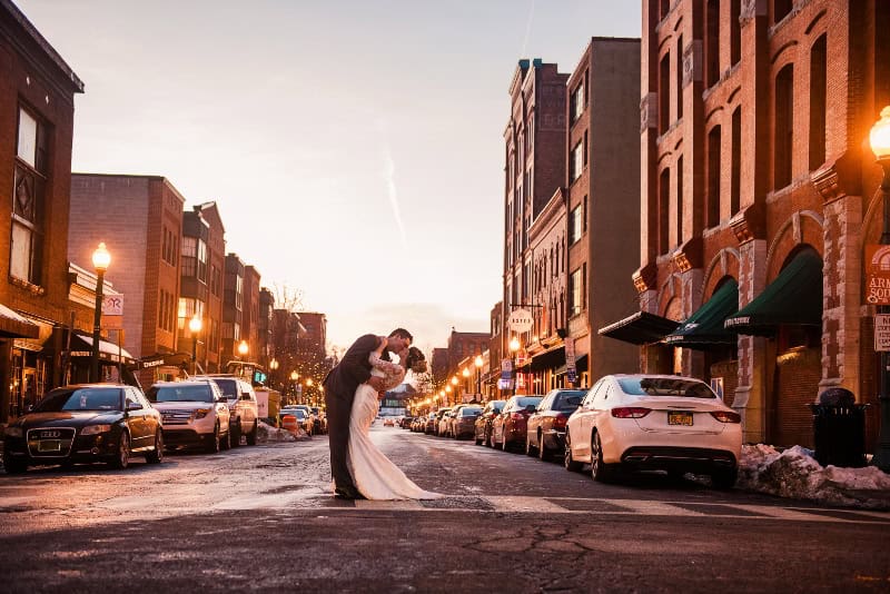 Bride and groom sharing a kiss on a city street during winter sunset.
