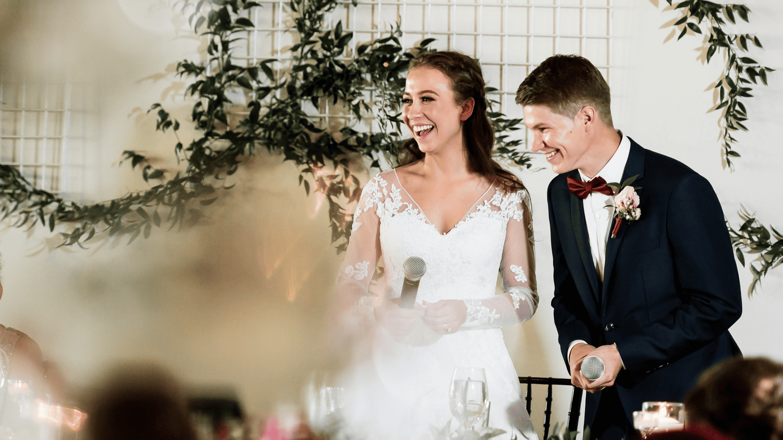Bride and groom smiling at wedding reception with microphones.