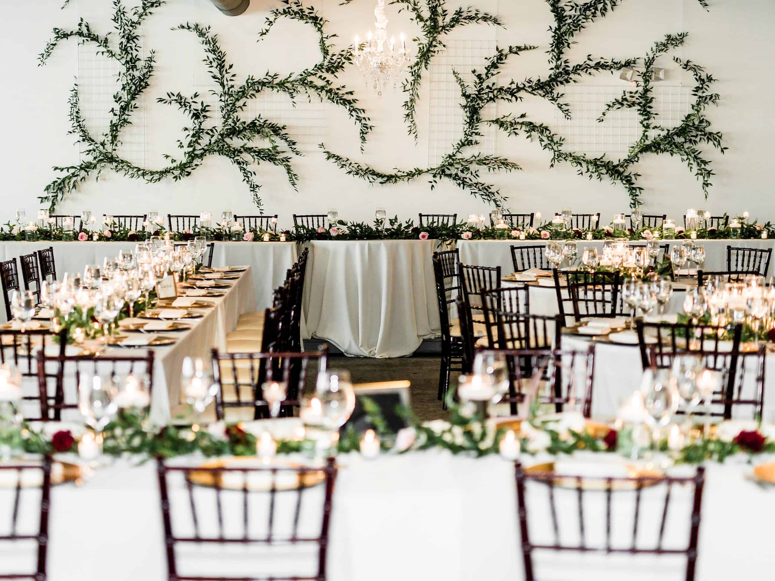 Wedding reception with decorated tables, greenery, and ambient lighting.