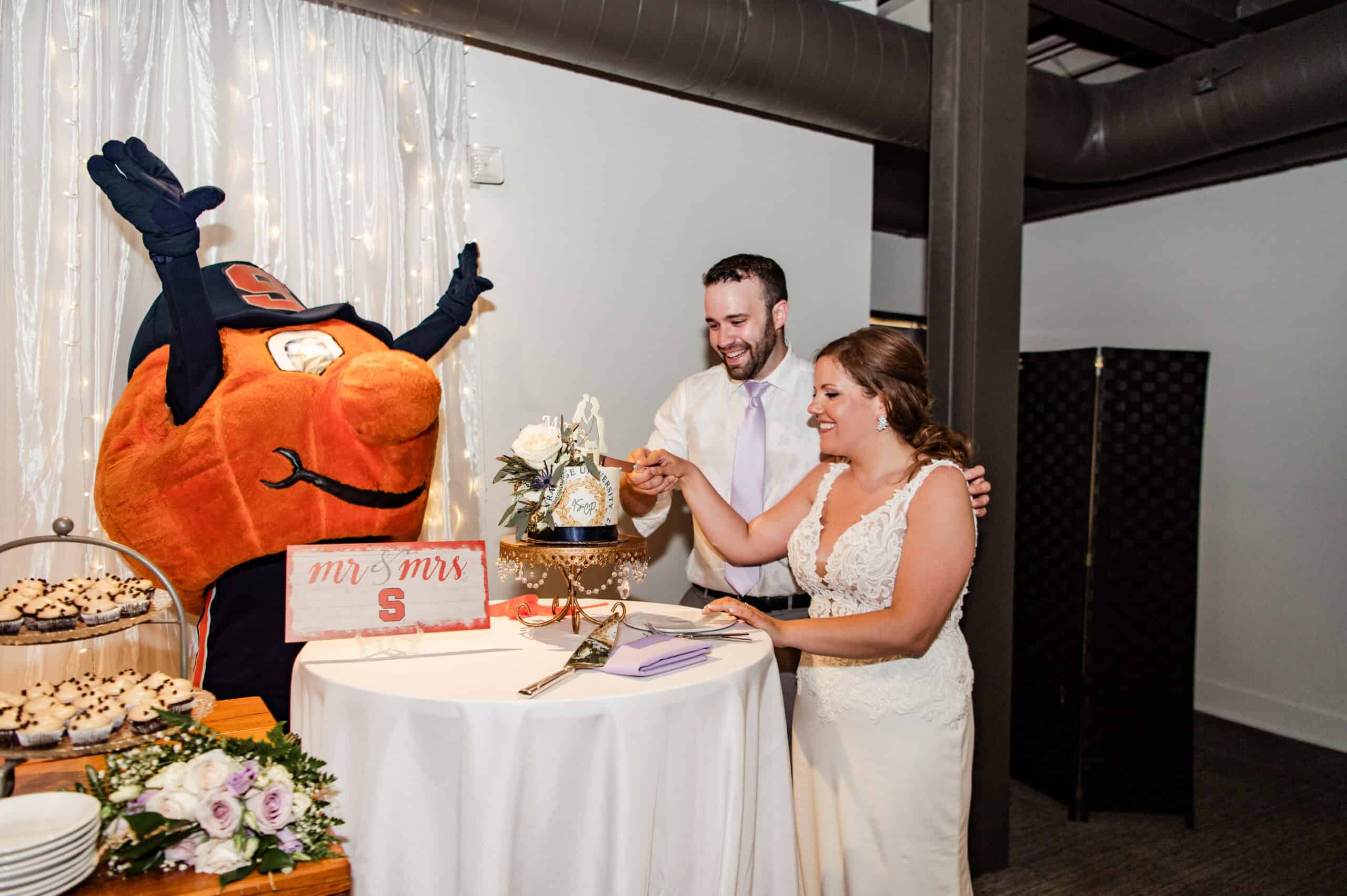 Bride and groom cutting wedding cake with mascot at SKY Armory event.