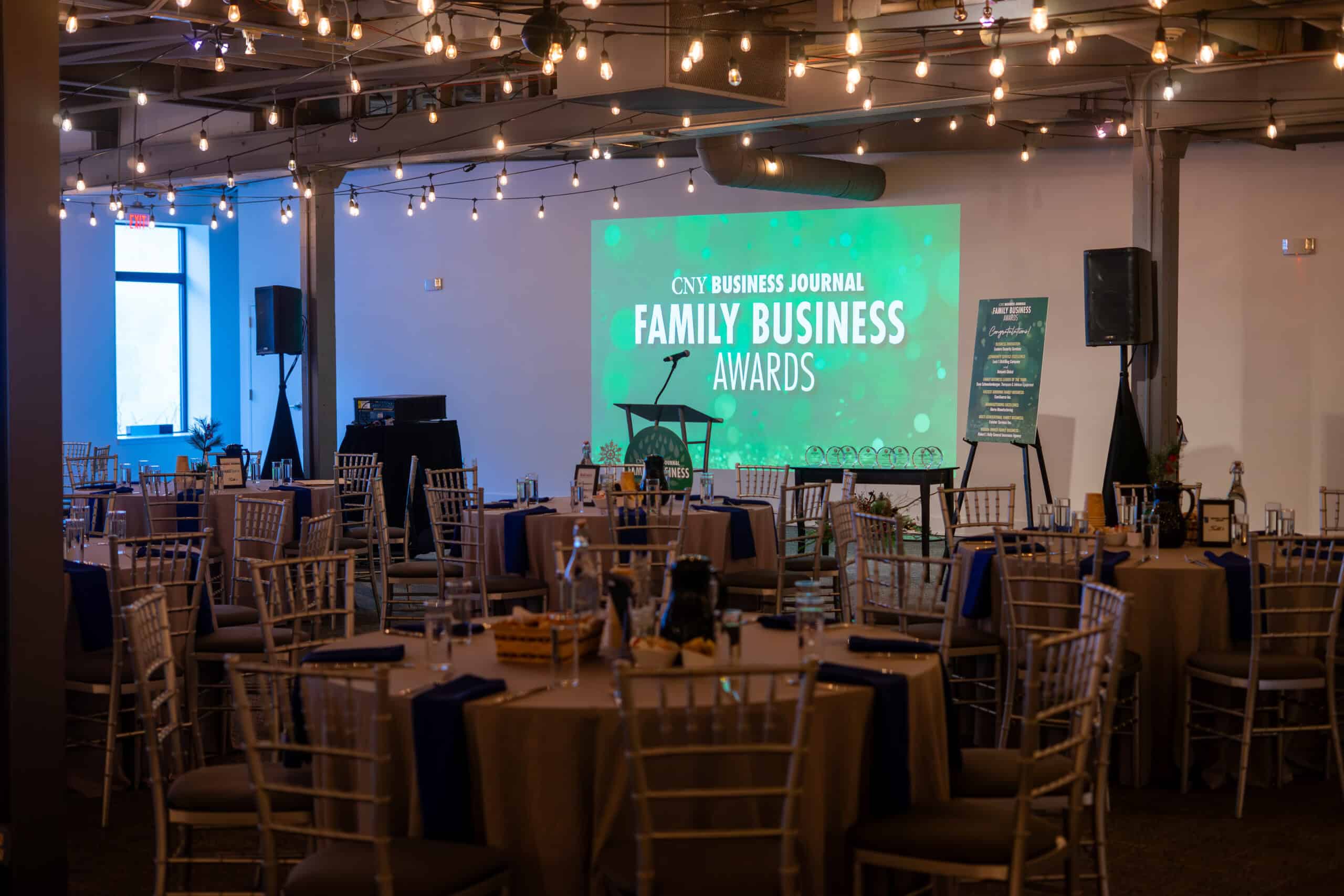 Event setup with tables, chairs, and a large screen for Family Business Awards.