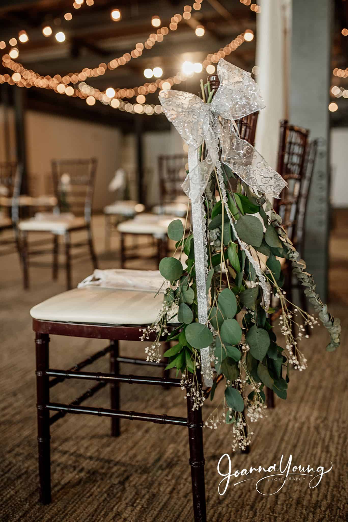 Wedding chair decorated with greenery and a lace bow for elegant event decor.