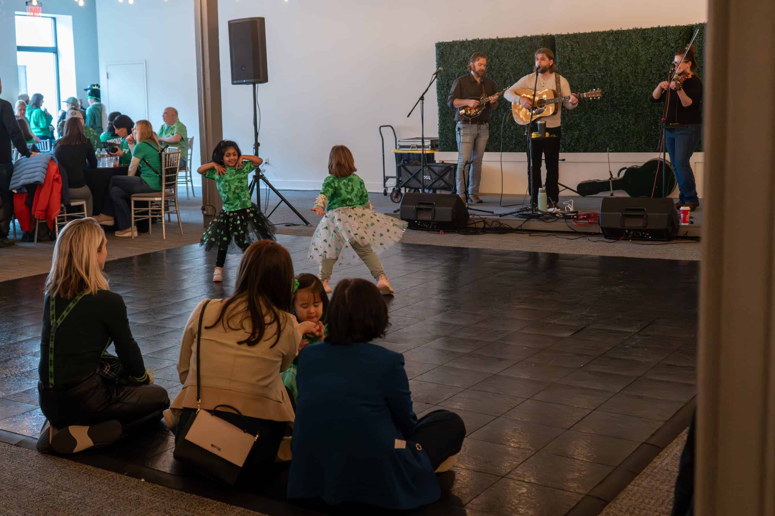 Musicians performing live on stage with children dancing in front.