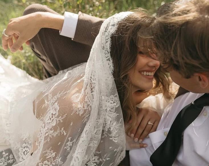 Bride and groom sharing a joyful moment outdoors with lace veil and wedding attire.