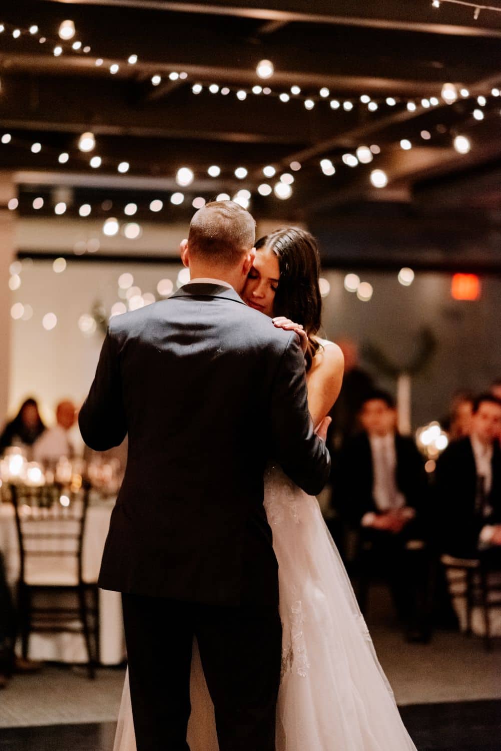 Bride and groom dancing at wedding reception with string lights overhead.